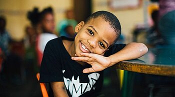 Enfant souriant ayant la tête posée sur son bras.