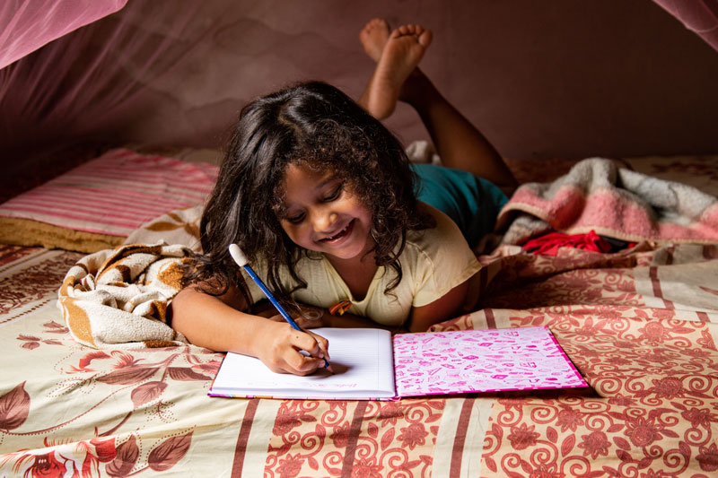 Petite fille souriante, écrivant dans son cahier.