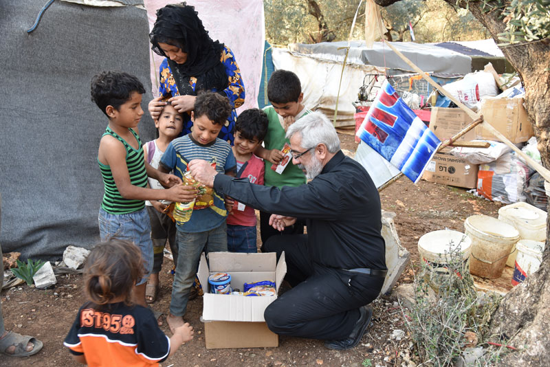 Homme distribuant des denrées alimentaire à un groupe d'enfants, accompagné d'une femme, dans un camp. 
