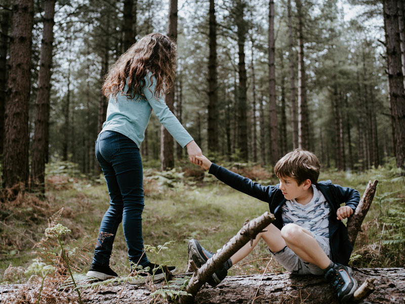 Petite fille tendant la main à un petit garçon pour l'aider à se relever dans une forêt.