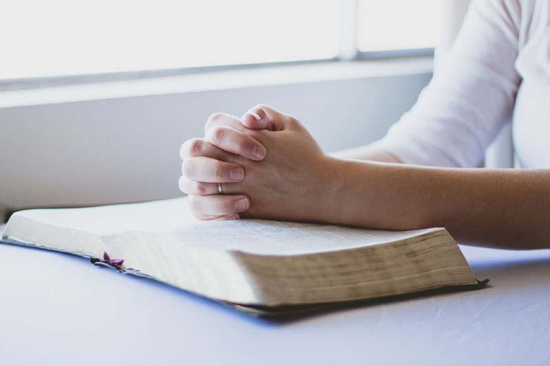 Image montrant une personne en train de prier les mains jointes sur une Bible ouverte.