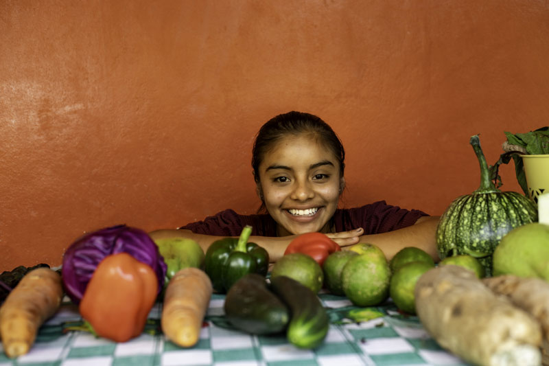 Image d'une jeune fille souriante entourée de légumes. 