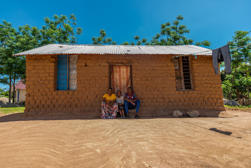 Image de trois personnes, assises devant une maison.