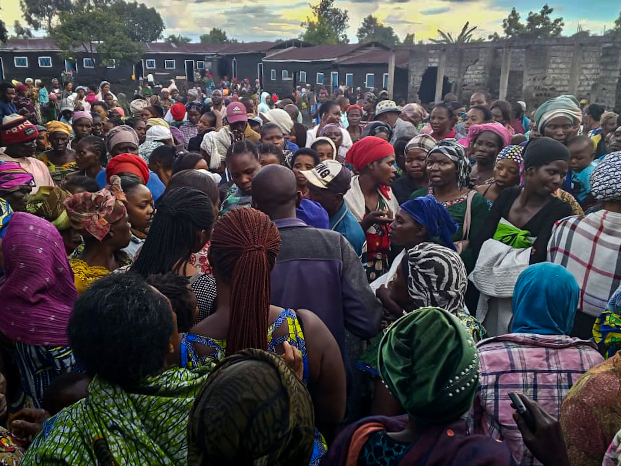 Groupe de personnes rassemblées à l’extérieur : principalement des femmes, devant des habitations modestes.