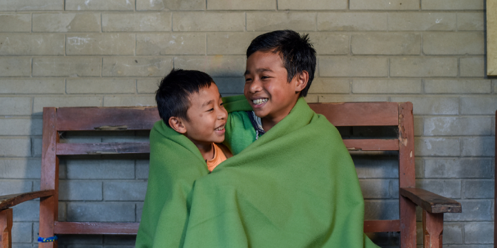 Deux jeunes garçons souriants sous une couverture. 