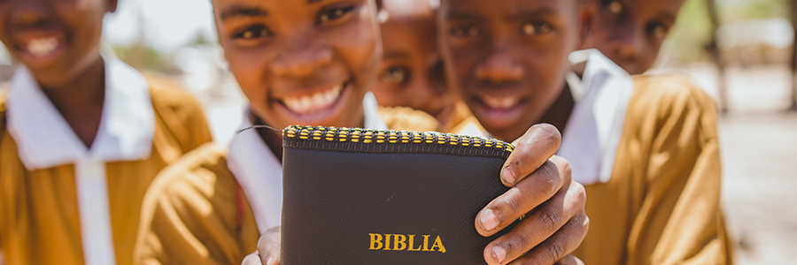 Enfant souriant montrant tendant une Bible vers l'objectif.